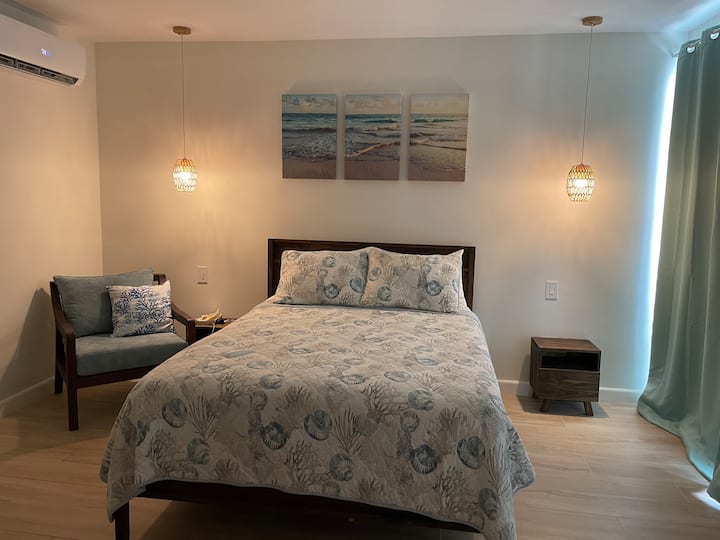 Master bedroom with ocean-themed bedding, woven pendant lamps, and beach triptych art
